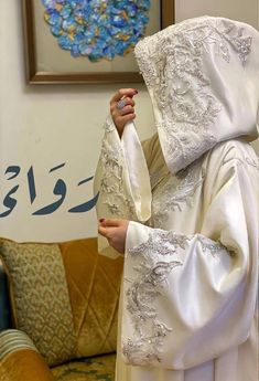 a woman wearing a white dress and veil in front of a painting on the wall