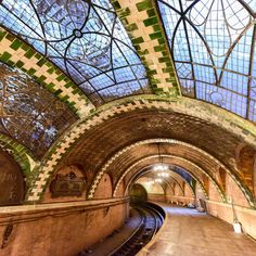 the inside of a train station with green and white tiles on the ceiling, along with tracks