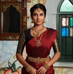 a woman in a red and gold sari with jewelry on her neck, posing for the camera