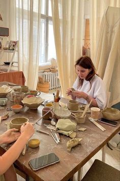 two women sitting at a table making bowls and spoons with pottery on the table