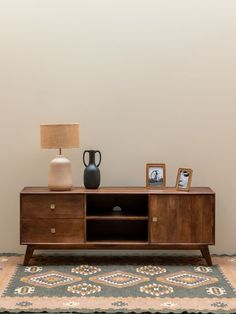 a sideboard with two vases on it next to a lamp and photo frames