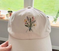 a white hat with flowers embroidered on the front and side, sitting in front of a window