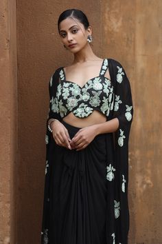 Black floral embroidered cape with split sleeves. Comes with padded bustier and draped skirt.
Components: 3
Pattern: Embroidery
Type Of Work: Sequins, Cutdana, Mirror, Zari, Beads
Neckline: Cape: Open, Bustier: Sweetheart
Sleeve Type: Cape: Split, Bustier: Sleeveless
Fabric: Uppada Silk, Georgette, Crepe
Color: Black
Other Details: 
Attached lining
Closure: Skirt: Button
Approx weight (in kgs): 2-3
Occasion: Sangeet - Aza Fashions Evening Set With Cape Sleeves, Evening Sets With Cape Sleeves, Embroidered Sets With Cape Sleeves For Evening, Evening Sets With Draped Sleeves In Georgette, Evening Pre-draped Saree With Cape Sleeves, Embroidered Evening Sets With Cape Sleeves, Embroidered Evening Set With Cape Sleeves, Evening Sets With Embroidered Cape Sleeves, Fitted Cape Sleeves Blouse For Party