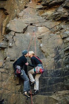 two people climbing up the side of a rock face each other with ropes attached to their backs