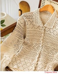 a crocheted sweater sitting on top of a chair next to a wooden hanger