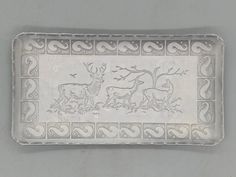 a decorative silver tray with deer and tree designs on the front, sitting on a gray surface