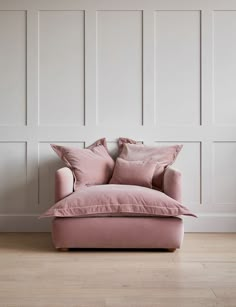 a pink chair sitting in front of a wall with white paneling and wooden floors