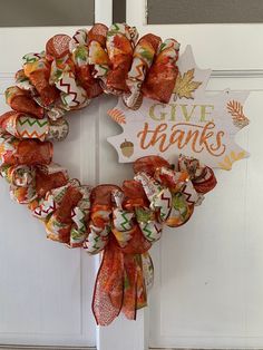 a thanksgiving wreath on the front door with give thanks written in orange, green and white