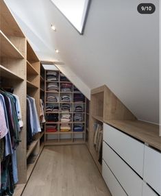 an attic closet with white drawers and wooden shelves filled with shirts, pants and sweaters