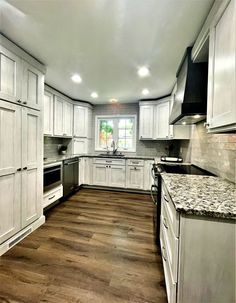 an empty kitchen with white cabinets and wood flooring on the walls, along with stainless steel appliances