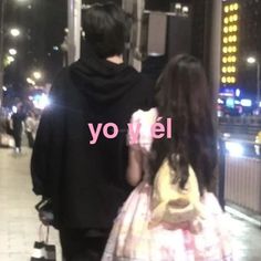 a man and woman walking down a street at night with their back to the camera