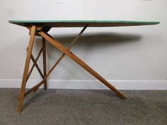 a wooden table with a green top on carpeted floor next to white wall and door