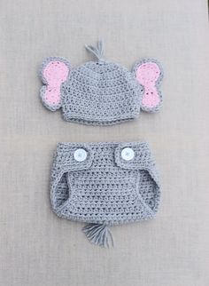 two crocheted hats and diaper covers are laying on a tablecloth, one is grey with pink ears