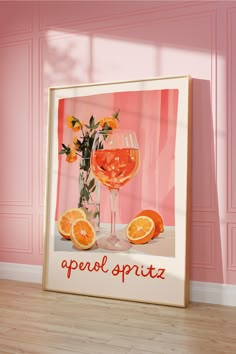 an orange and wine glass sitting on top of a wooden floor next to a pink wall