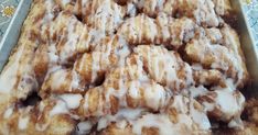 a pan filled with cinnamon rolls covered in icing on top of a blue table cloth