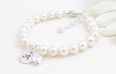 "Personalized real pearl bracelet for infant, baby or little girl: Created with gorgeous Grade-A round 5.5mm freshwater pearls, a durable sterling silver heart-shaped lobster clasp with a 1/2\" \"Grow with Me\" extender chain, a high quality 3/8\" round disc with one initial (4 font options to choose from), and a small sterling silver heart charm.  A small sparkling clear Swarovski® crystal is in between the two charms.  The charms can be placed front/center or near the clasp.  The pearls are st Dainty White Round Charm Bracelet, Classic White Heart-shaped Bracelet, Elegant Nickel-free Name Bracelet For Mother's Day, Elegant Hypoallergenic Name Bracelet With Round Beads, Classic White Bracelets For Mother's Day, Pearl White Sterling Silver Bracelet With Round Beads, Personalized Silver Pearl Bracelet For Wedding, Silver Pearl Bracelet With Pearl Charm For Mother's Day, Personalized Round Bead Pearl Bracelet In Elegant Style