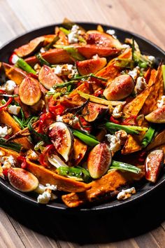 a black plate topped with lots of food on top of a wooden table