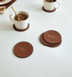 three coasters on a table with two cups of coffee and one slice of orange