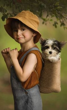 a young boy carrying a dog in a sack on his back while standing under a tree