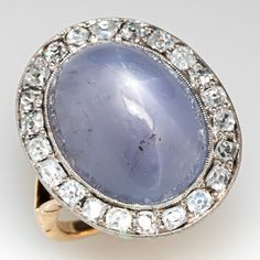 This marvelous circa 1900 platinum topped 18K yellow gold ring is centered with one (1) oval cabochon cut natural star sapphire set into a platinum bezel setting. The sapphire is bordered wit twenty-two (22) old mine cut diamonds bead set into platinum bezel setting. The ring measures 22.7mm at the top, rises 9.6mm above the finger, tapering to 1.7mm wide and 1.0mm thick at the base of the shank. The ring is currently a size 6.5. The ring shows some overall wear and the stone shows light abrasio Luxury Oval Cabochon Sapphire Wedding Ring, Luxury Round Sapphire Ring With Bezel Setting, Luxury Vintage Sapphire Ring With Polished Finish, Luxury Oval Cabochon Wedding Ring, Luxury Vintage Sapphire Cabochon Ring, Fine Jewelry Platinum Sapphire Cabochon Ring, Platinum Sapphire Cabochon Ring In Fine Jewelry Style, Platinum Cabochon Sapphire Ring Fine Jewelry, Formal Platinum Sapphire Cabochon Ring