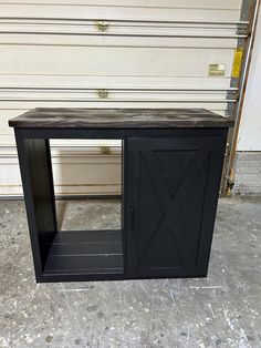 a small black cabinet sitting on top of a cement floor next to a garage door