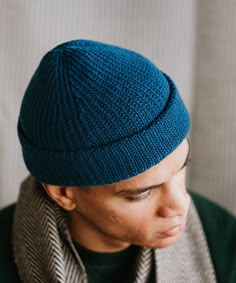 a man wearing a blue knitted hat with a scarf around his neck and looking down