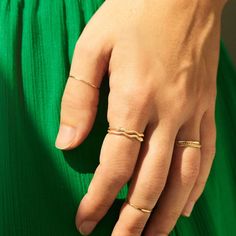 A hand rests in front of vibrant green fabric. The hand is wearing dainty gold rings stacked on eachother for a bolder look. Gold Midi Rings With A Modern Twist, Stackable Fine Jewelry Midi Rings, Modern Twist 14k Gold Stackable Rings, Yellow Gold Midi Rings In Recycled Gold, Adjustable Recycled Gold Stackable Rings, Stackable Midi Rings In Recycled Gold, Elegant 14k Gold Snake-shaped Ring, Elegant 14k Gold Snake Shaped Rings, Gold Tiny Midi Rings Fine Jewelry