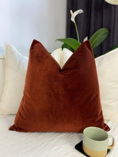 a brown pillow sitting on top of a white bed next to a cup and saucer