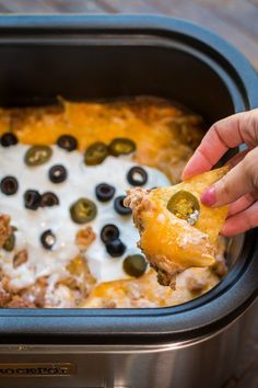 a person dipping some olives into a casserole dish