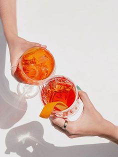 two people holding drinks in their hands with orange slices on the rims and one has an orange slice