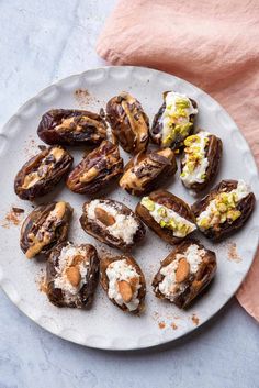 a white plate topped with stuffed dates covered in cheese and nuts next to a pink napkin