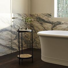 a white bathtub sitting next to a window in a bathroom with marble walls and floors