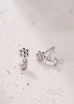 Made from solid 925 sterling silver, these are small stud earrings that have a delicate metallic flower with six 'petals' that sits on the ear lobe, a tiny square zirconia hanging underneath and silver butterfly clasps. Compact, with a timeless design, these studs will pair well with other delicate hoops or studs. 🎁 Packaging: Beautifully packed in a box, ready for gifting. 🏷️ This product is made of sterling silver -- easily recognizable by its '925' stamp of authenticity. It is also hypoallergenic, making it suitable for people with sensitive or irritable skin. We recommend avoiding perfume, deodorant or other chemicals. Details: ✅ Material: 925 sterling silver with 18k gold plated, cubic zirconia ✅ Available in gold and silver ➕ Purchase extra earring backs to make sure your favorite Silver Minimalist Dangle Flower Earrings, Silver Dangle Flower Earrings Minimalist Style, Dainty Sterling Silver Single Flower Earring, Tiny Sterling Silver Flower Earrings, Silver Cubic Zirconia Flower Earrings, Silver Flower Drop Earrings In Fine Jewelry Style, Silver Drop Flower Earrings In Fine Jewelry Style, Silver Cubic Zirconia Flower Earrings As Gift, Silver Cubic Zirconia Flower Earrings For Gift