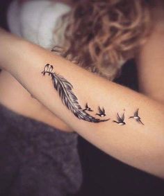 a woman with a tattoo on her arm that has birds flying around it and a feather in the middle