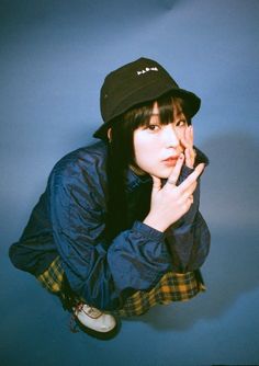 a young woman wearing a black hat and blue jacket posing for the camera with her hand on her mouth