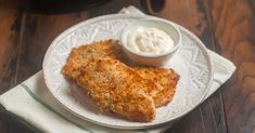 two pieces of fried chicken on a white plate with a small bowl of sour cream