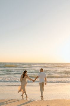 a man and woman holding hands while walking on the beach