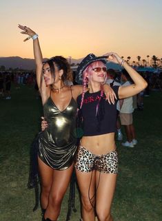 two women dressed up in costumes posing for the camera at an outdoor music festival with their arms around each other