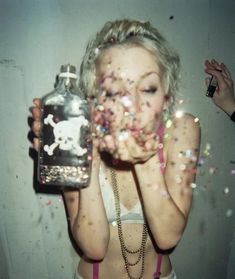 a woman holding a bottle with confetti all over her face and hands in front of her face