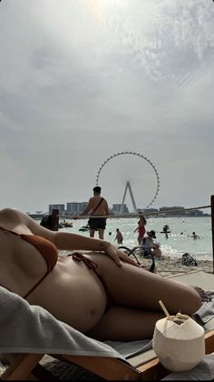 a woman laying on top of a beach next to a ferris wheel in the background