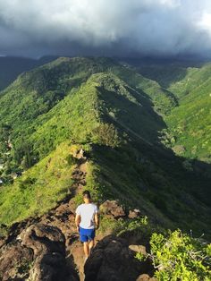 a man walking up the side of a mountain on top of a lush green hillside