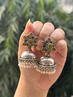 These high quality German silver earrings are the perfect addition to any ethnic or western look. The stone used reflects light and gives a look of mystery and allure to your outfit. These earrings will last you forever and are sure to be your go to pair! Plus they came in an adorable flower shape!  Available in 4 stunning colours, these earrings need to be in your collection!  They are limited edition and unique styles so only 1 of each is available and will not be restocked in the future, so grab yours today!  In case of any query, please feel free to reach out to us. Happy shopping! Bohemian Silver Dual-tone Earrings, Bohemian Silver Bridal Earrings With Latkans, Silver Jhumkas For Navratri, Bohemian Bridal Earrings With Latkans In Silver, Bohemian Bridal Silver Earrings With Latkans, Bohemian Sterling Silver Drop Jhumkas, Sterling Silver Bohemian Jhumkas, Silver Dual-tone Round Earrings, Traditional Silver Flower Earrings For Festive Occasions