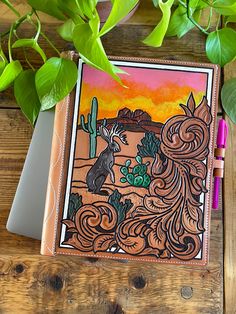 a notebook with an image of a desert scene on it next to some green plants