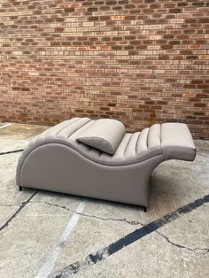 a grey leather chaise lounge chair sitting in front of a brick wall and floor