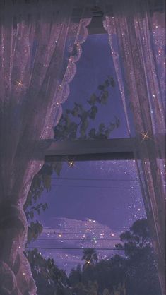 a window with curtains and lights shining in the night sky above it, as seen from outside