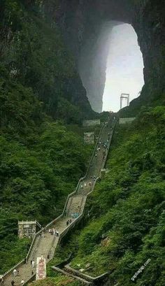 an aerial view of a tunnel in the mountains with people walking up it and on top