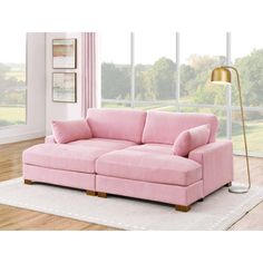 a pink couch sitting on top of a white rug in a living room next to a window