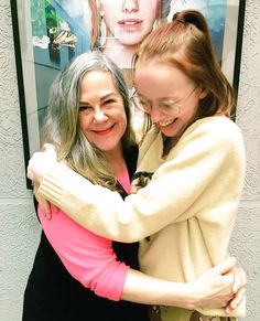 two women hugging each other in front of a poster