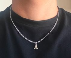 a person wearing a black shirt with a silver chain necklace on their neck and the letter a in the middle