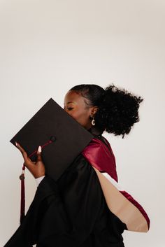 a woman in a graduation gown holding a black book with a tassel on it